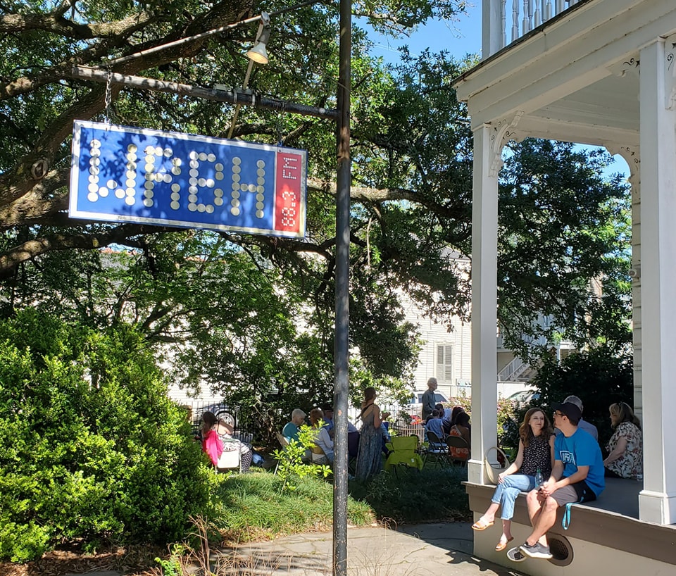 WRBH Reading Radio People sitting on the porch of the WRBH Reading Radio studio on Magazine Street in New Orleans with the WRBH logo sign shown on a warm, sunny spring day.